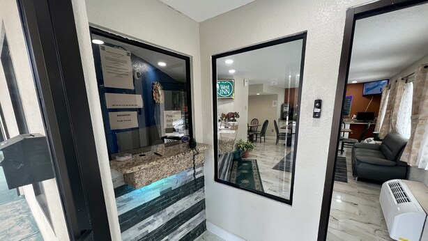 A hotel reception area with a marble counter, a large mirror, and a view into the dining area. - Key West Inn - Roanoke (Roanoke)