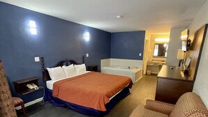 A hotel room with a bed, a chair, a small table, a desk, a mirror, and a bathroom visible through an open door. - Key West Inn - Roanoke (Roanoke)