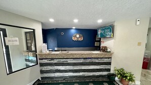 A reception area with a counter, a clock, a welcome sign, and a small potted plant. - Key West Inn - Roanoke (Roanoke)