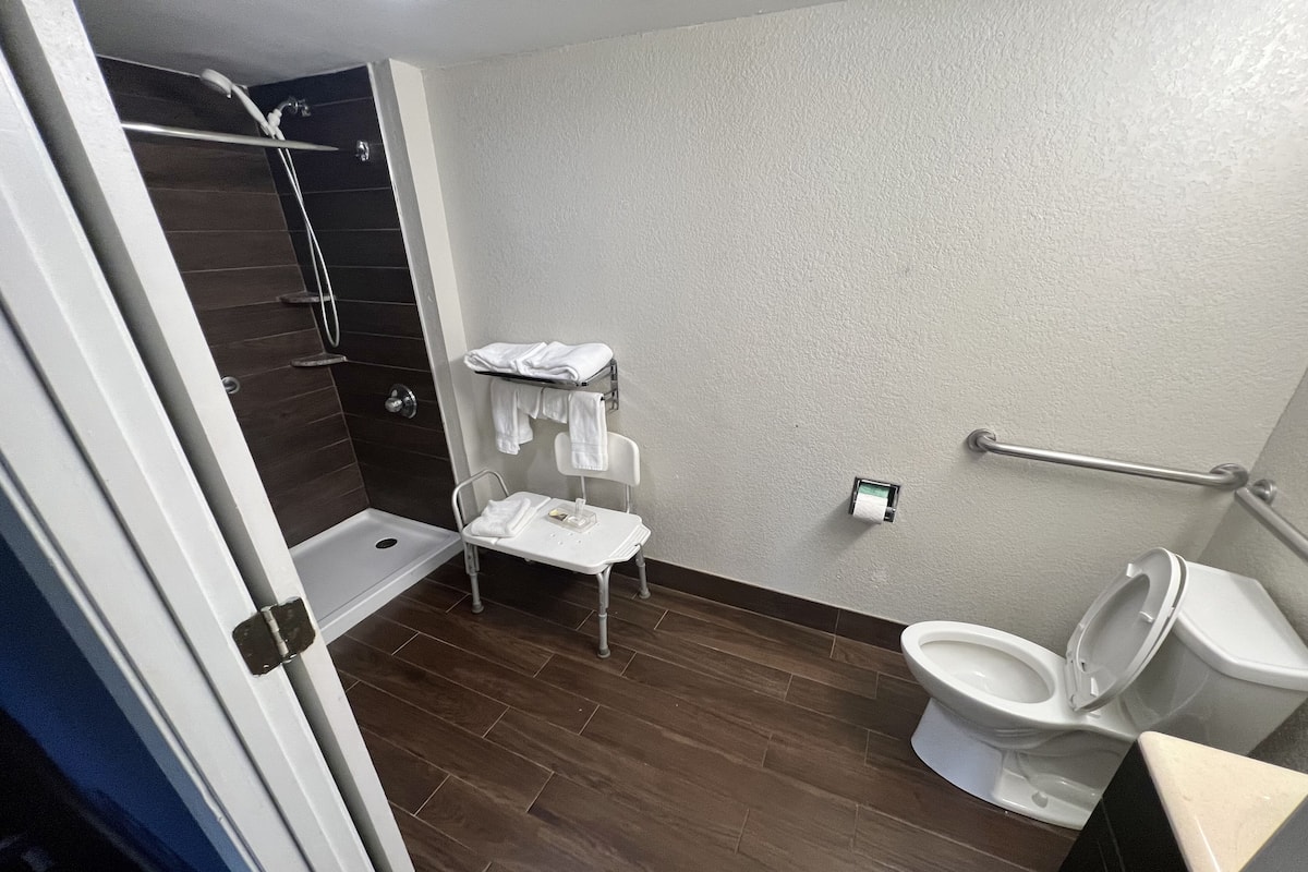 A bathroom with a shower, a toilet, a sink, and a small chair.