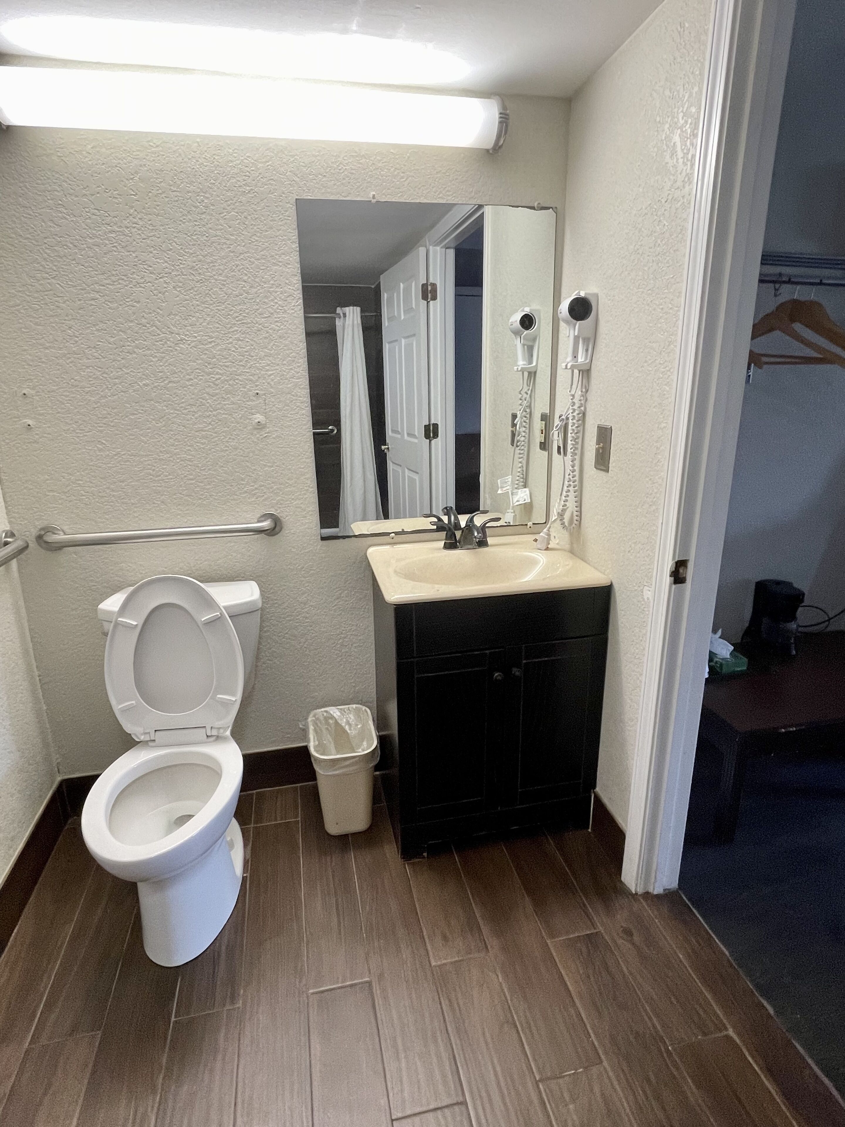 A bathroom with a white toilet, a sink with a mirror, and a trash bin.
