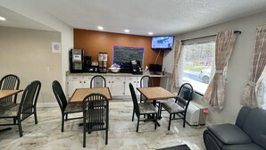 A dining area with a table and chairs, a coffee machine, a television, and a window with curtains. - Key West Inn - Roanoke (Roanoke)