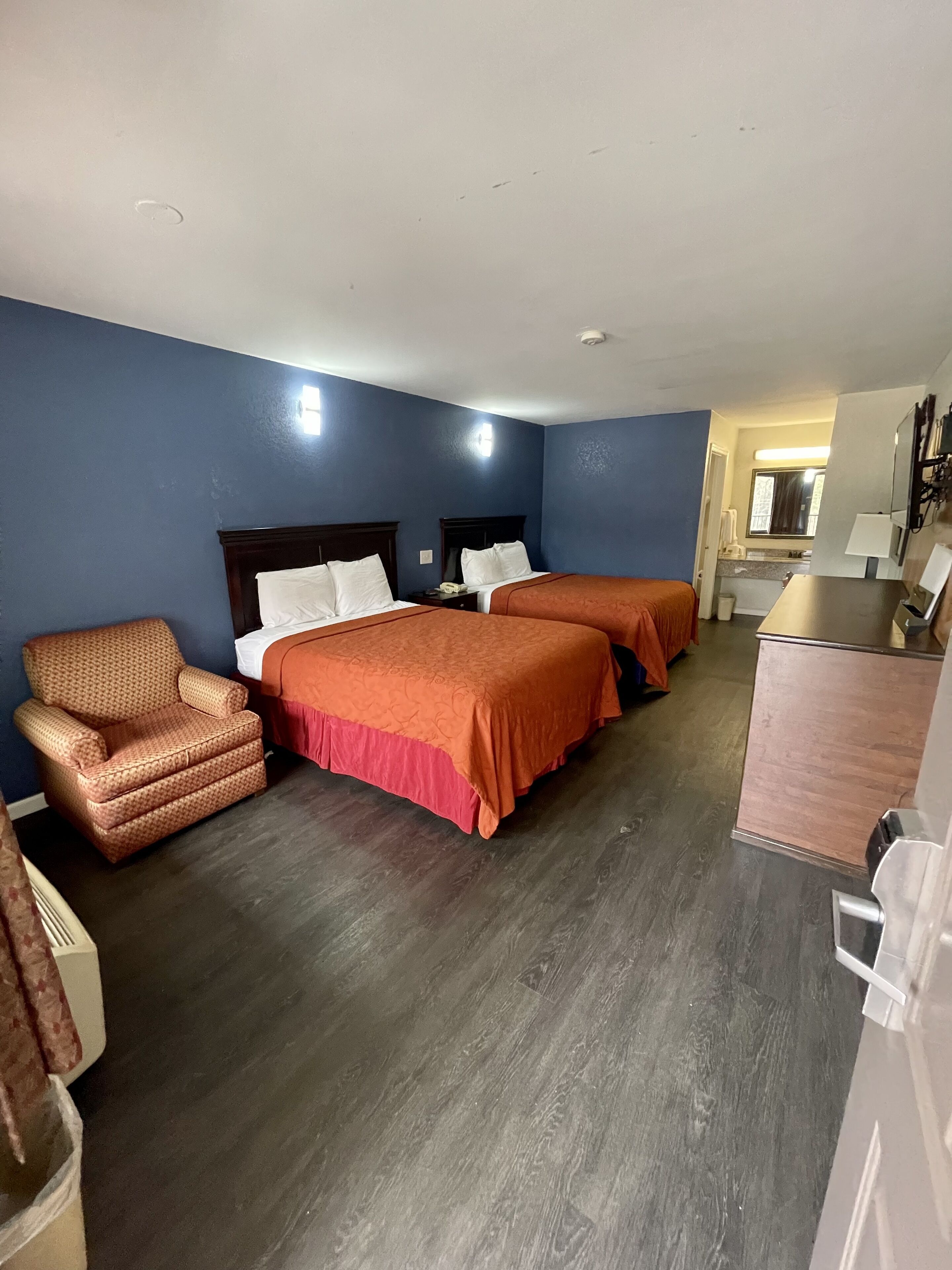 A hotel room with two beds, a chair, a desk, and a mirror.