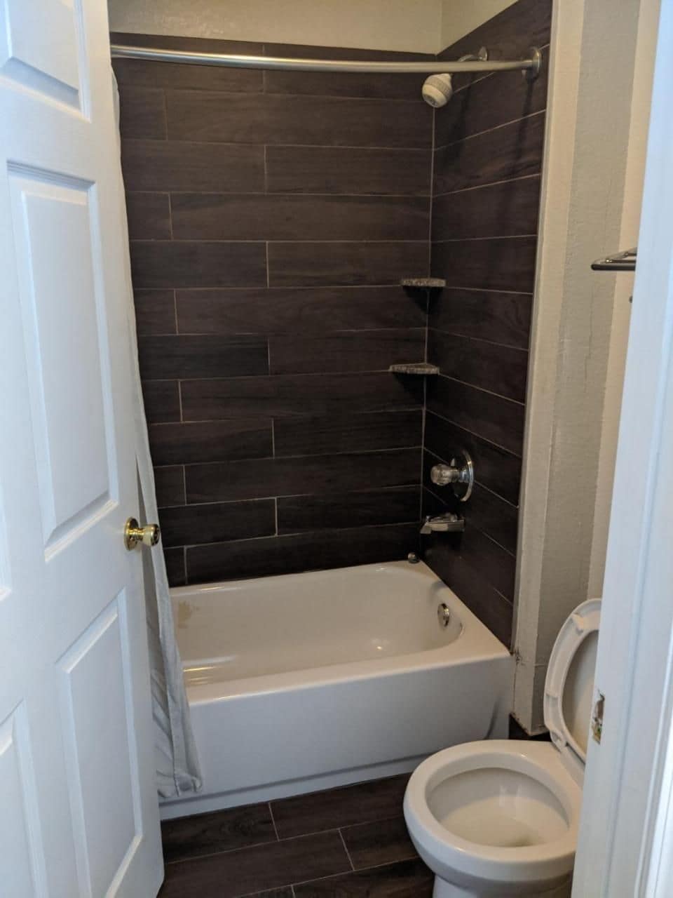Ein Badezimmer mit einer Badewanne, einer Toilette und dunkel gefliesten Wänden.