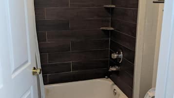 Ein Badezimmer mit einer Badewanne, einer Toilette und dunkel gefliesten Wänden.