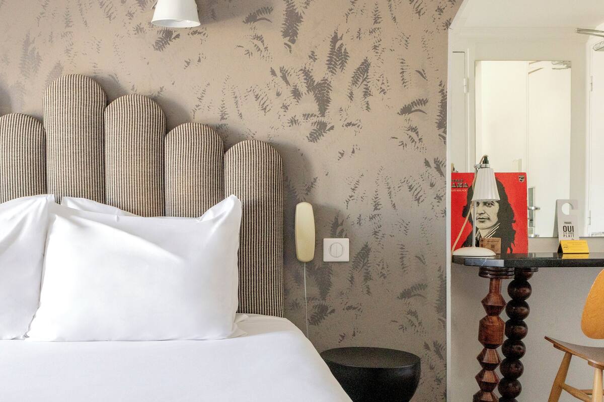 Een hotelkamer met een bed, hoofdeinde, bureau met lamp, stoel en spiegel.