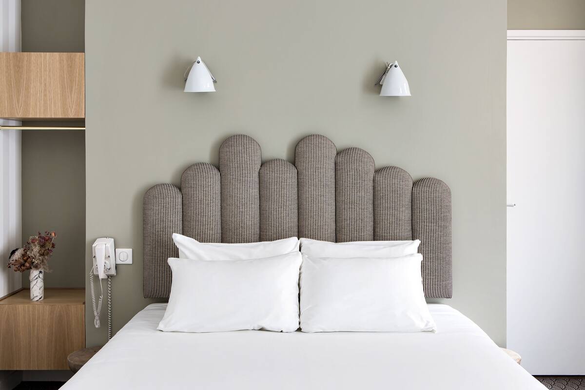 Een netjes ingerichte hotelkamer met een bed, twee bedlampen, een telefoon en een tafeltje met een bloemenvaas.