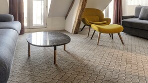 Een modern loft appartement met een hoge plafond, zichtbare houten balken, een grijze bank, een gele fauteuil en een ronde salontafel.