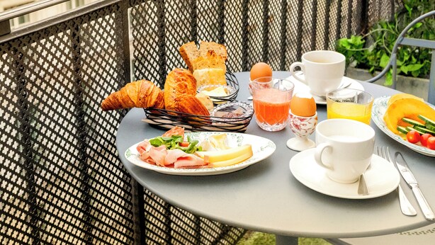 Een balkon met een ontbijttafel, compleet met croissants, eieren, sap en een bord met ham en kaas.