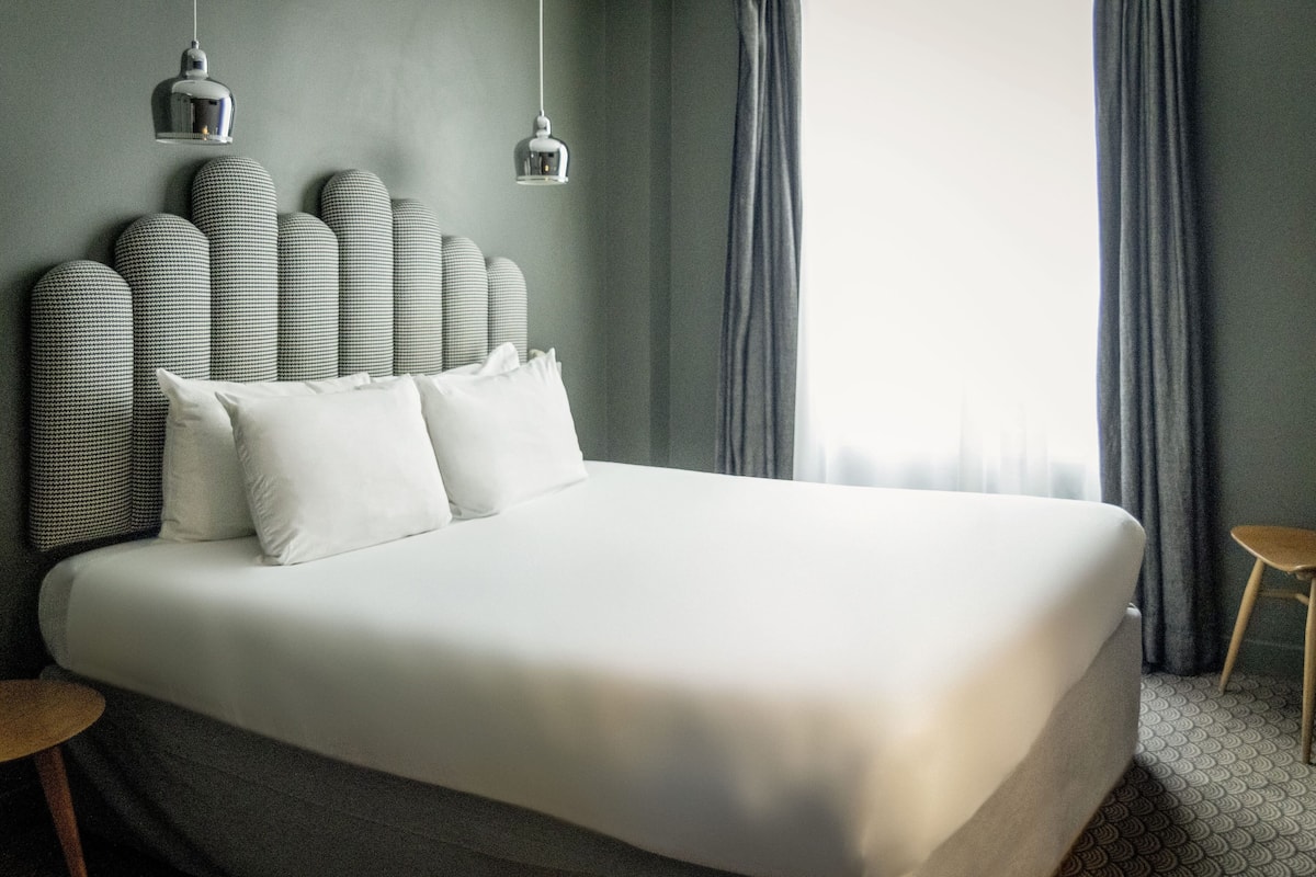 Een groot bed met hoofdeinde, twee bedlampen en uitzicht op een raam met gordijnen.