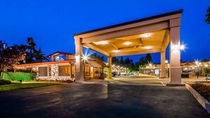 A hotel entrance with a covered parking area, a Best Western sign, and a stone facade building.