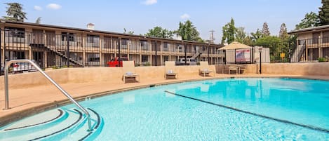 A swimming pool with lounge chairs and a building with balconies in the background.