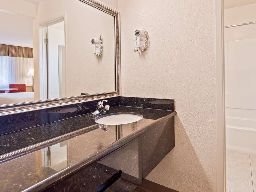 A modern bathroom with a black marble sink, a large mirror, and two wall-mounted hair dryers.