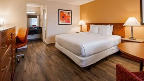 A hotel room with a bed, desk, chair, and a painting on the wall.