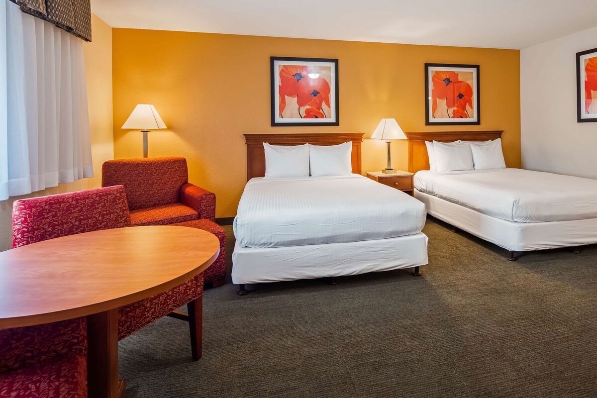 A hotel room with two beds, a red armchair, a round table, and two lamps.