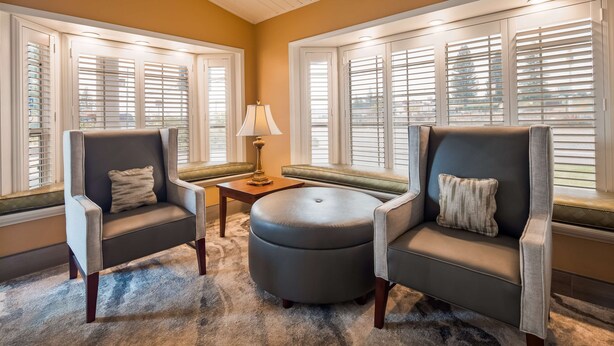 A cozy seating area with two armchairs and a round ottoman, a small table with a lamp, and a bench with a cushioned seat.