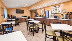 A restaurant with multiple tables and chairs, a counter with a coffee machine, and a television mounted on the wall.