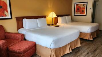 A hotel room with two beds, a red armchair, and a lamp.