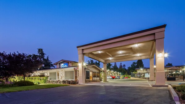 Um posto de gasolina com entrada coberta, placa Best Western e estacionamento com carros.
