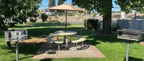 Un área de picnic con una mesa y bancos, rodeada de árboles y un césped.