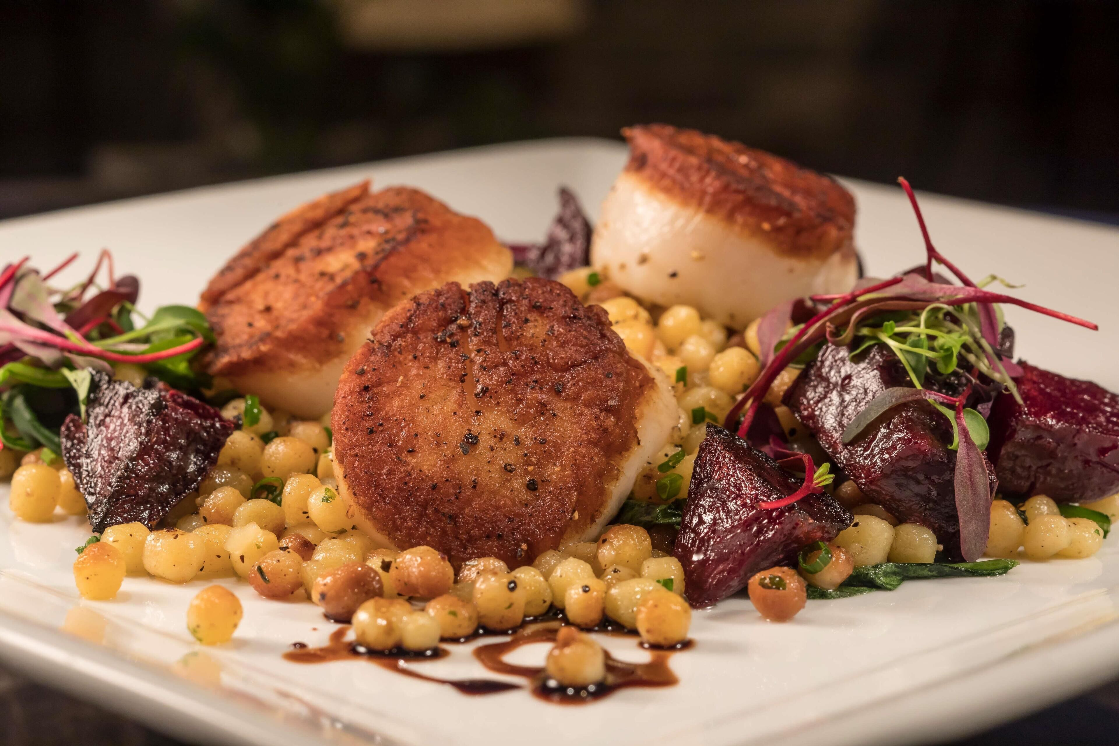 A plate of food with scallops, corn, and greens.