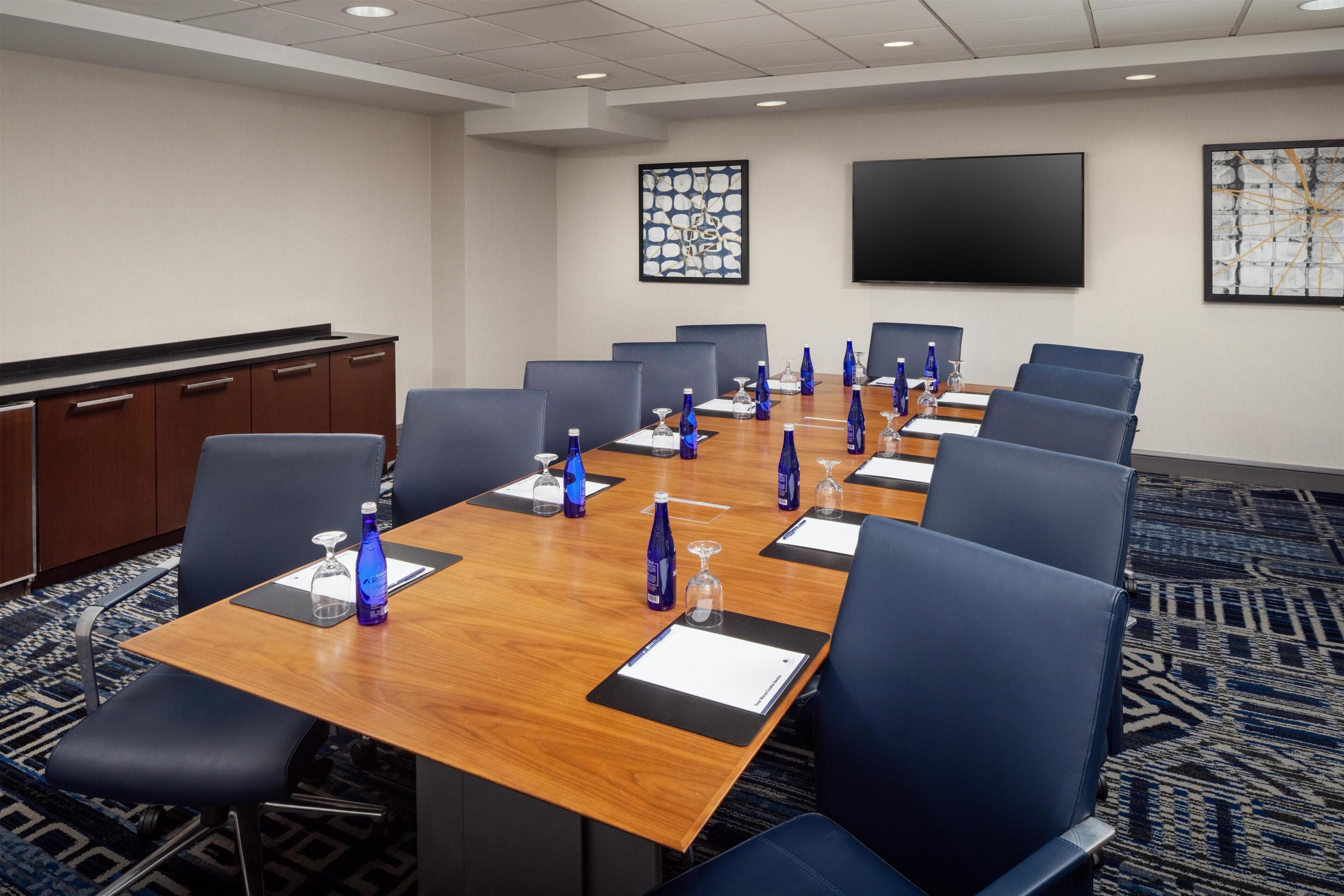 A conference room with a long table, blue chairs, and a TV screen on the wall.