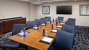A conference room with a long table, blue chairs, and a TV screen on the wall.