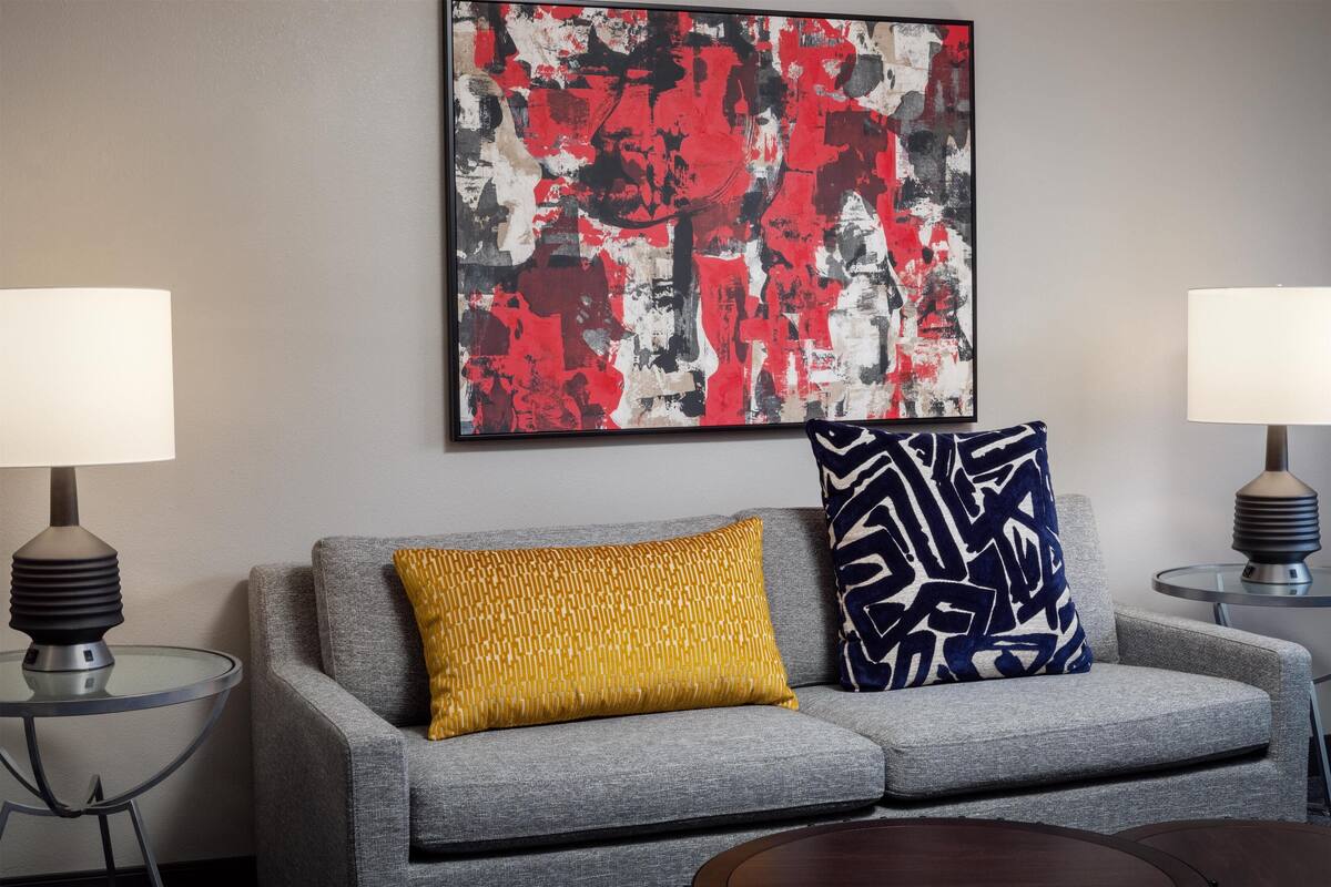 En moderne stue med en grå sofa, to mønstrede puder, et stort abstrakt maleri og to bordlamper på hver side.