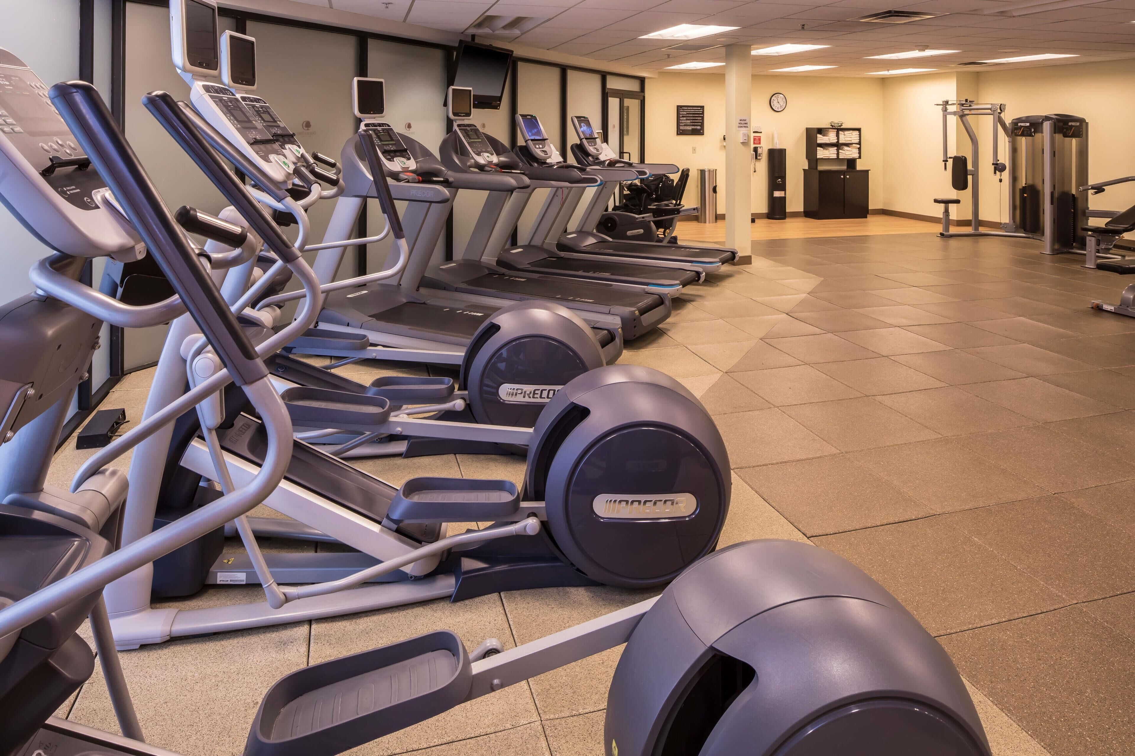 A row of treadmills in a gym with a tiled floor and exercise equipment in the background.