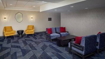 A hotel lobby with a geometric patterned carpet, two yellow armchairs, a blue sofa with red cushions, and a dark coffee table.