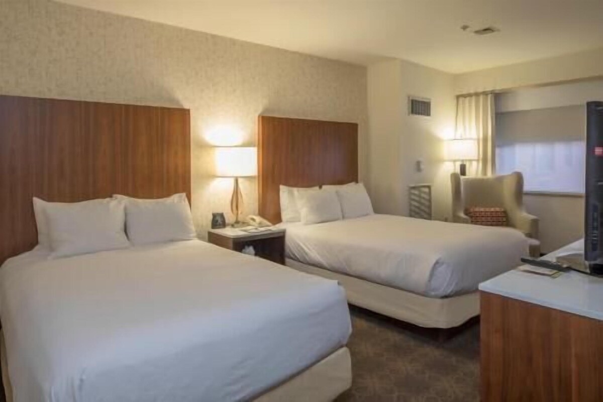 A hotel room with two beds, a desk, a chair, and a TV.