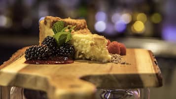 A dessert on a wooden board with a slice of cheesecake, blackberries, raspberries, and mint leaves.