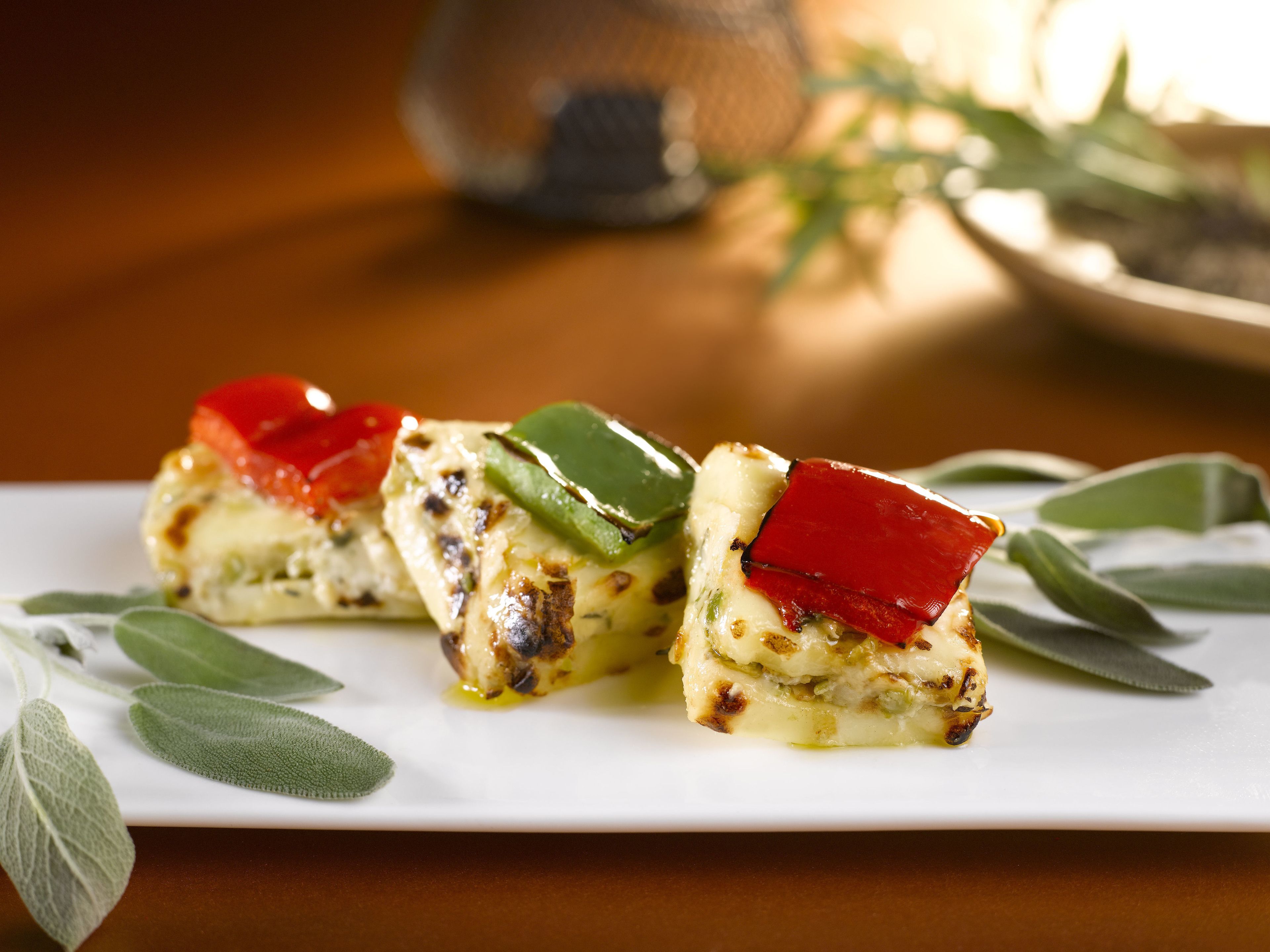 A white rectangular plate with three pieces of food, garnished with green leaves and red peppers.