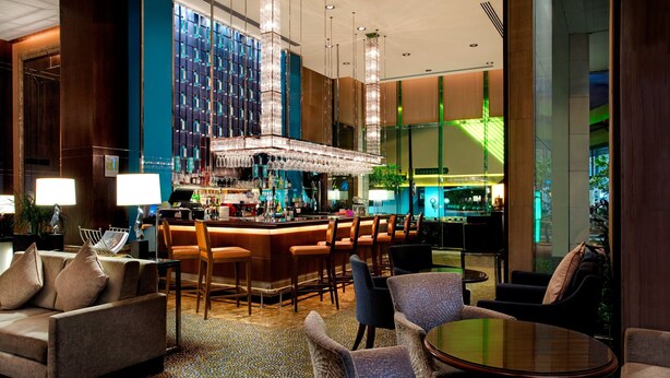A modern bar area with a high ceiling, bar stools, and a large chandelier. - Holiday Inn Singapore Orchard City Centre by IHG (Singapore)