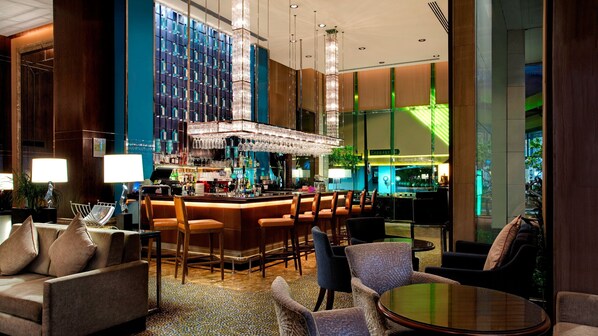 Uma área de bar moderna com teto alto, banquetas e um grande candelabro.