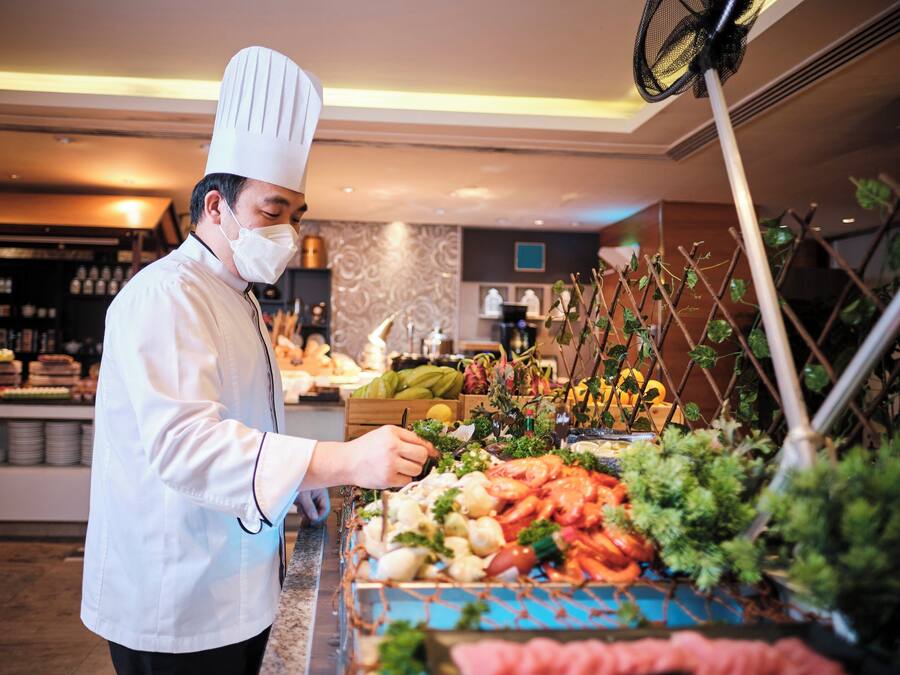 A buffet setup with various food items and a chef in uniform.