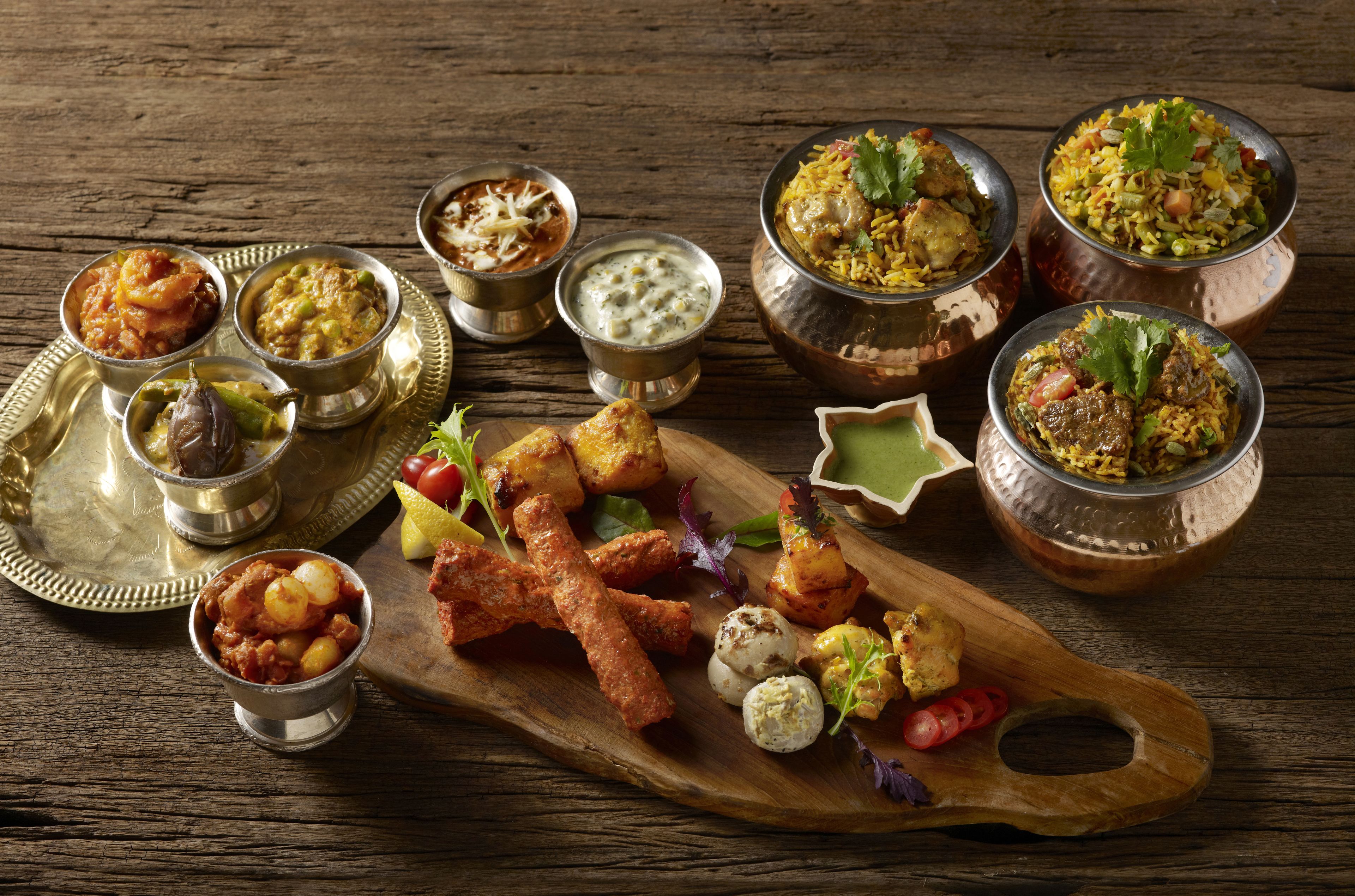 A variety of dishes including curries, rice, and grilled items on a wooden board.