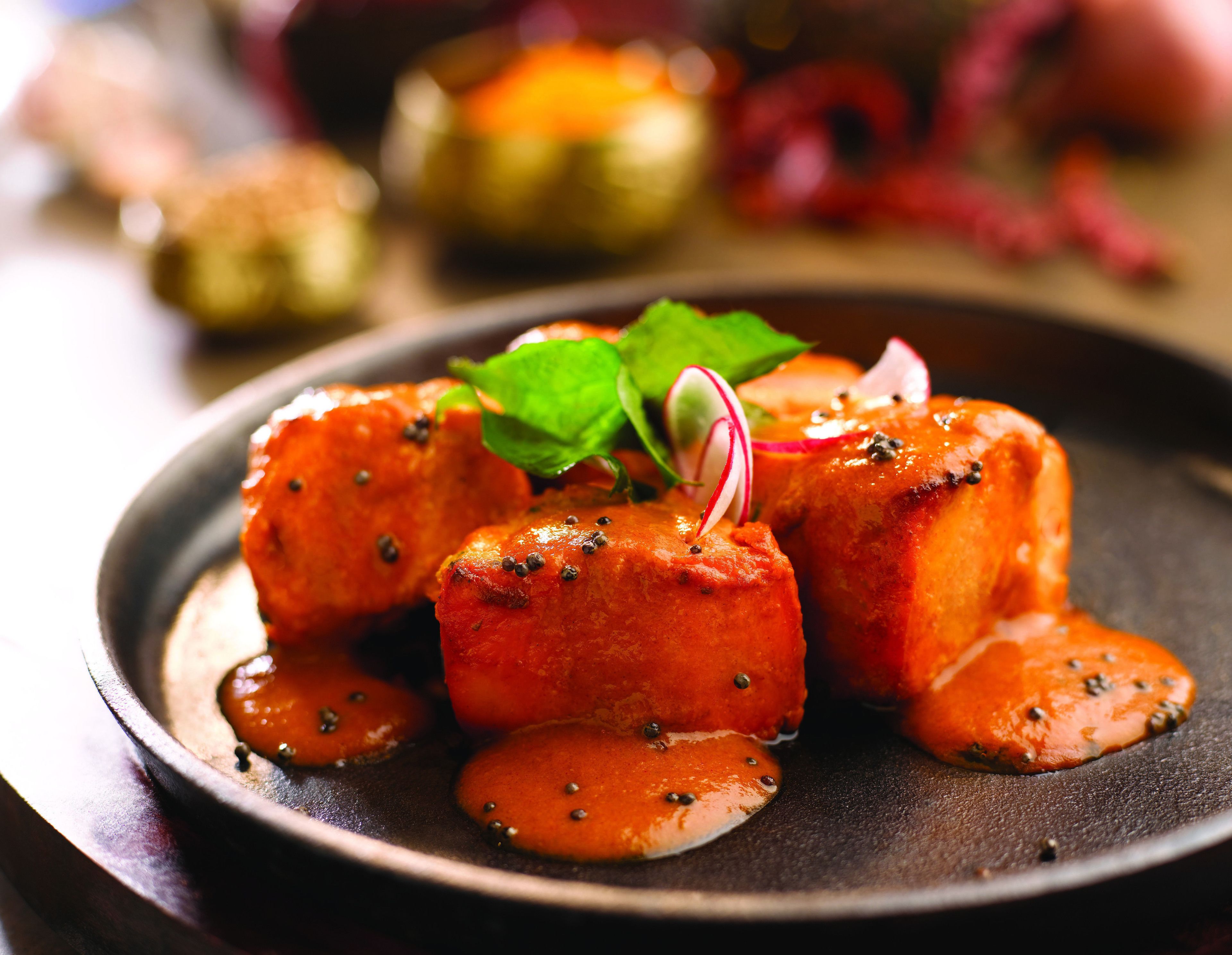 A dish of glazed meat with herbs and a sauce on a dark plate.