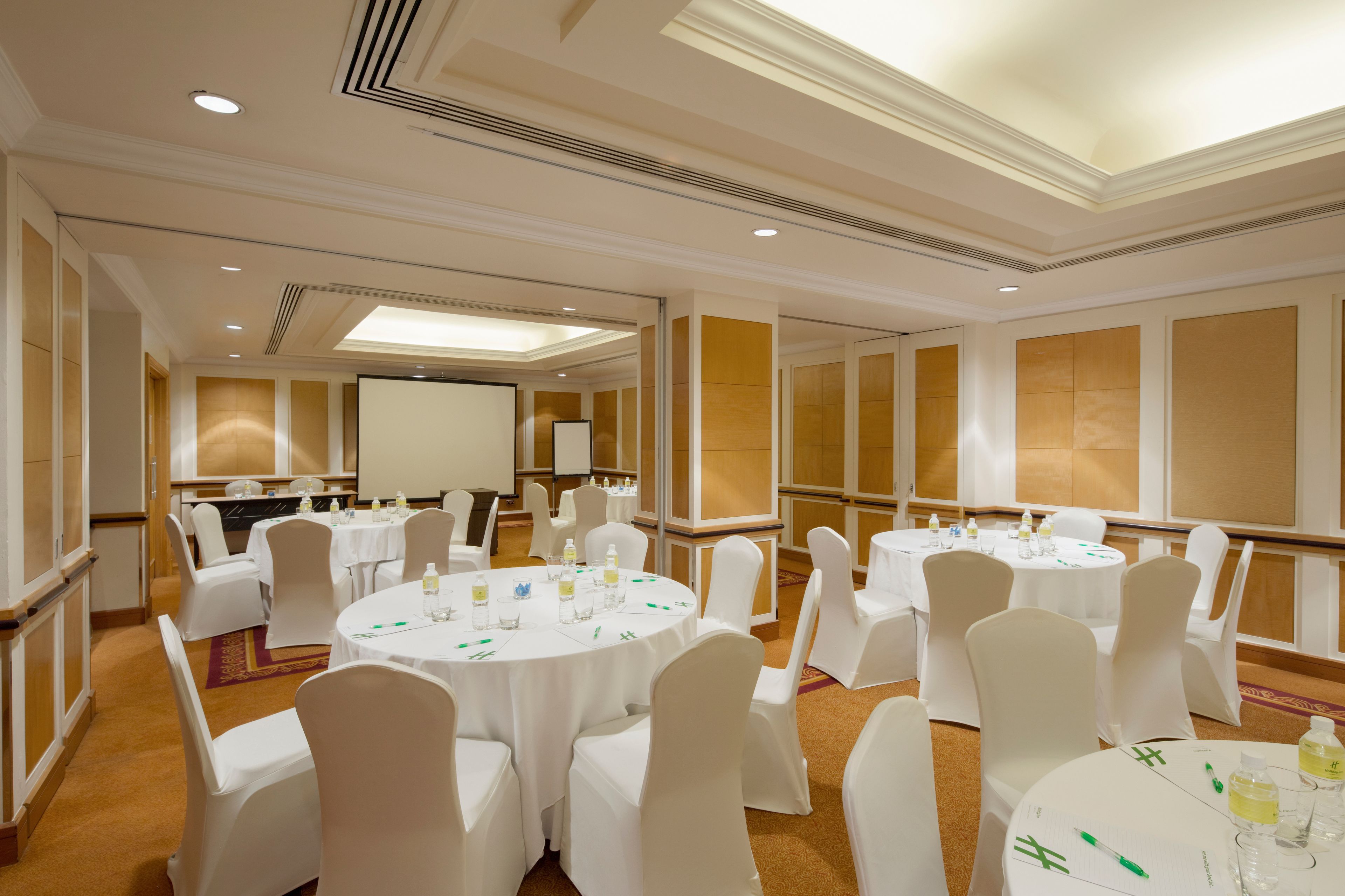 A conference room with multiple round tables and white chairs, equipped with water bottles and pens.