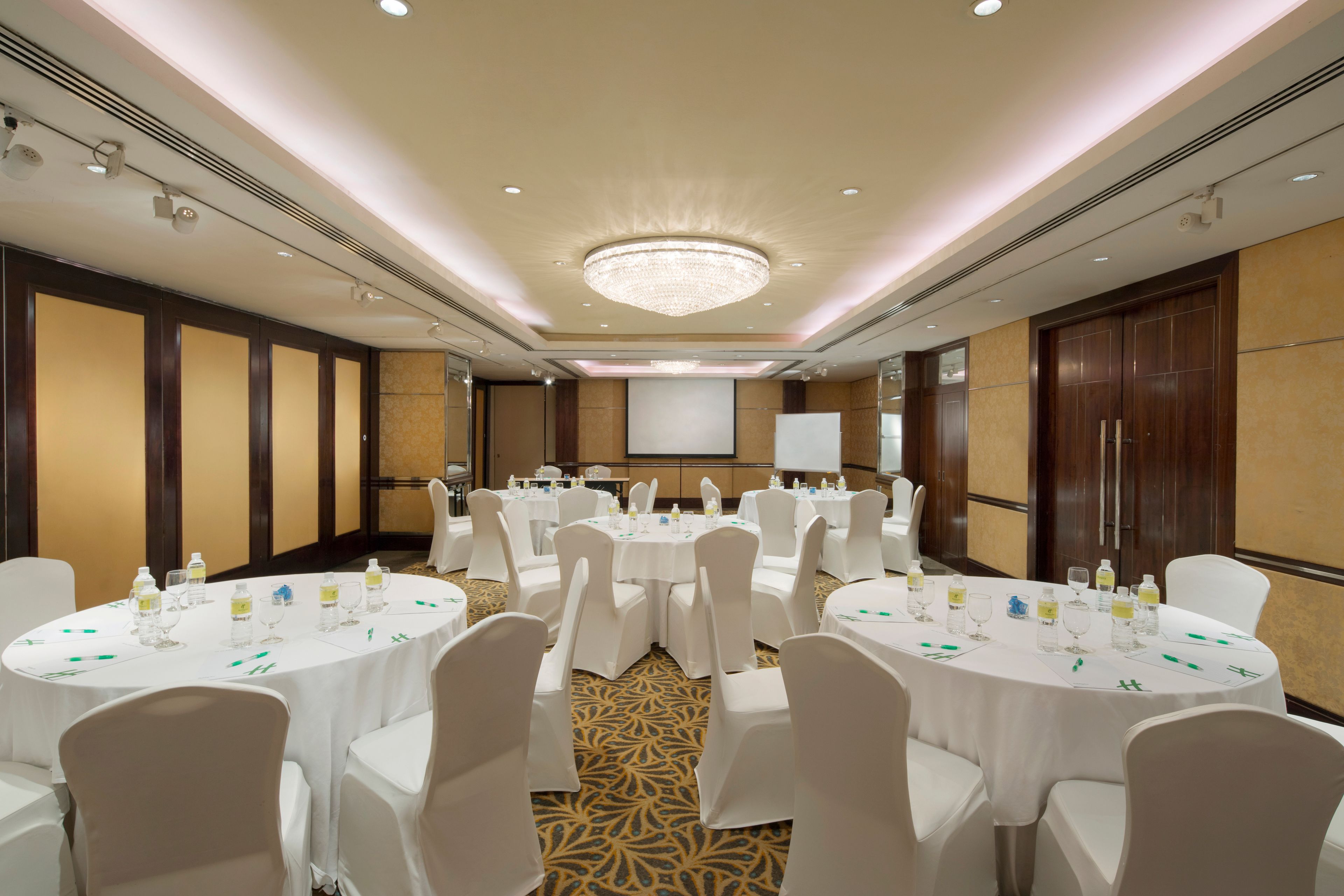 A conference room with round tables, white chairs, and a large chandelier.