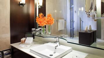A modern bathroom with a glass-topped sink, a large mirror, and a shower area.