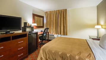 Une chambre d’hôtel équipée d’un lit, d’un bureau avec un ordinateur, d’une télévision, d’un four à micro-ondes et d’une lampe.