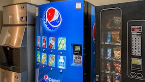 Máquina expendedora con logotipo de Pepsi, rodeada por un refrigerador de acero inoxidable.