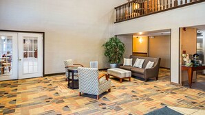 Un vestíbulo amplio con alfombra estampada, una zona de estar con sofá y sillones, una planta en maceta y una escalera que sube a un nivel superior.