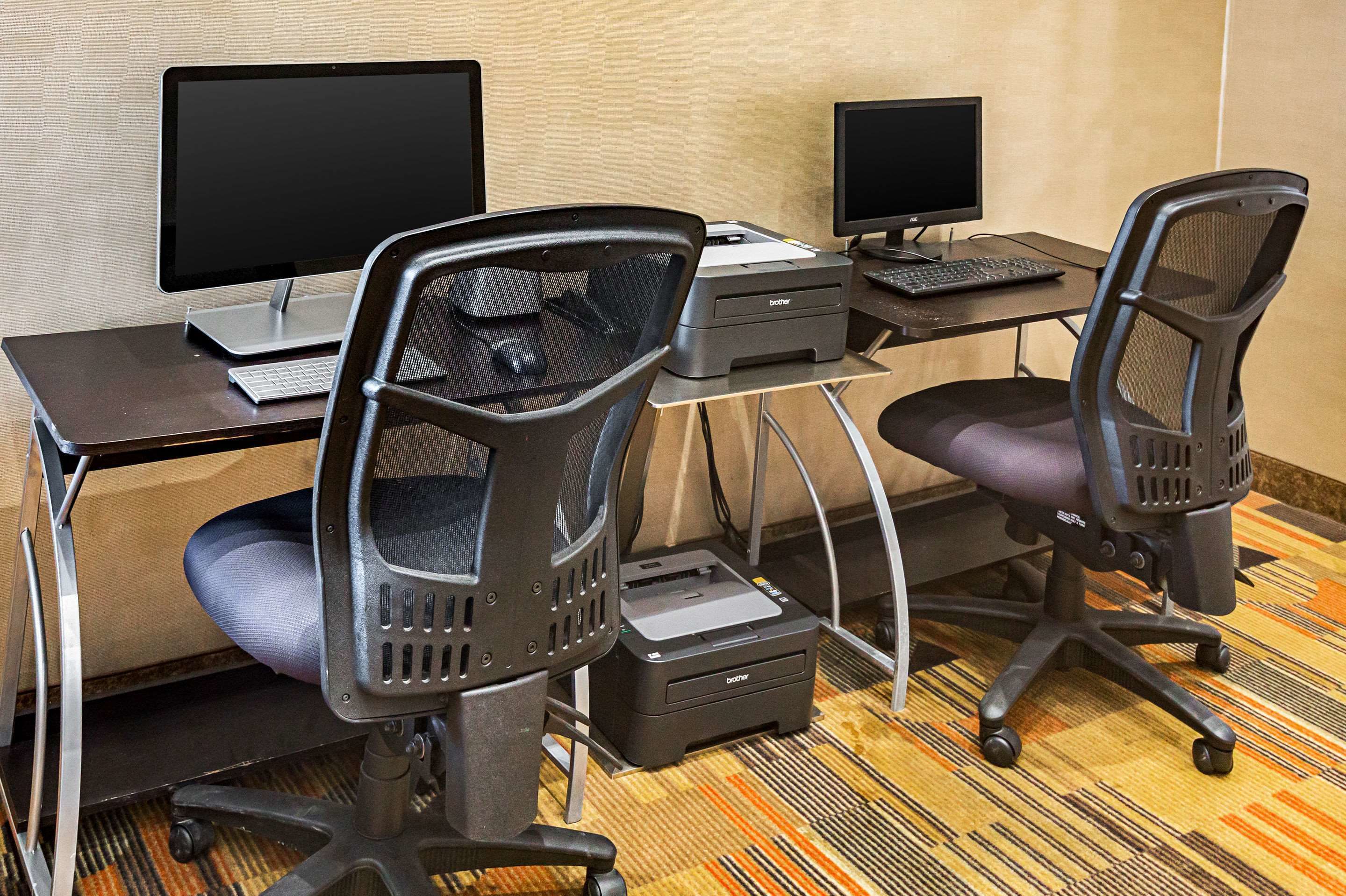 Een hotelwerkplek met twee bureaus, elk voorzien van een computermonitor, toetsenbord en printer.
