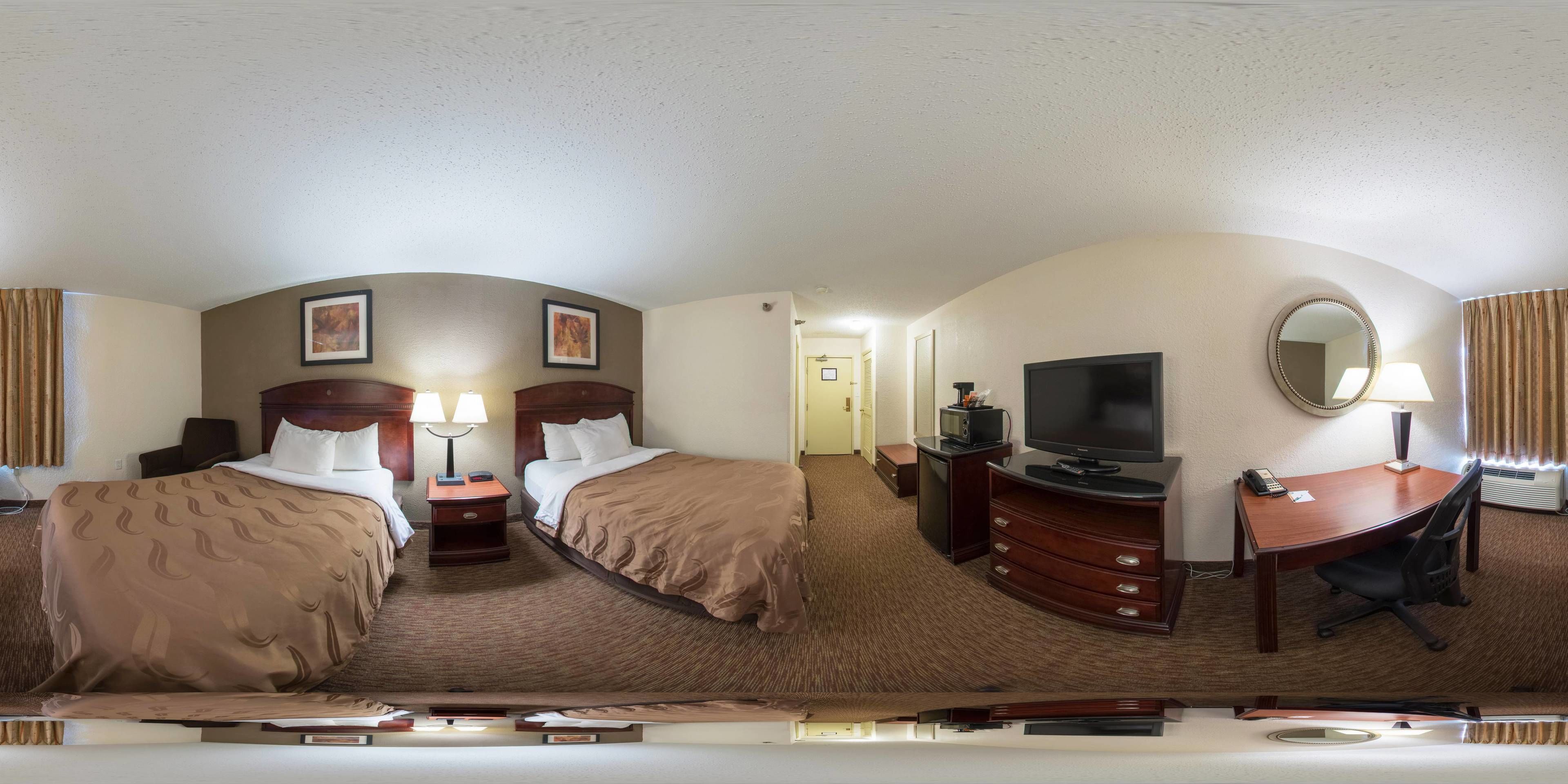 A hotel room with two beds, a desk with a TV, a mirror, and a dresser.