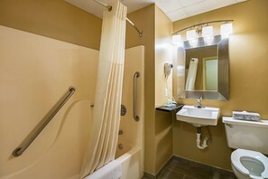 A bathroom with a shower, grab bars, a sink, and a toilet.