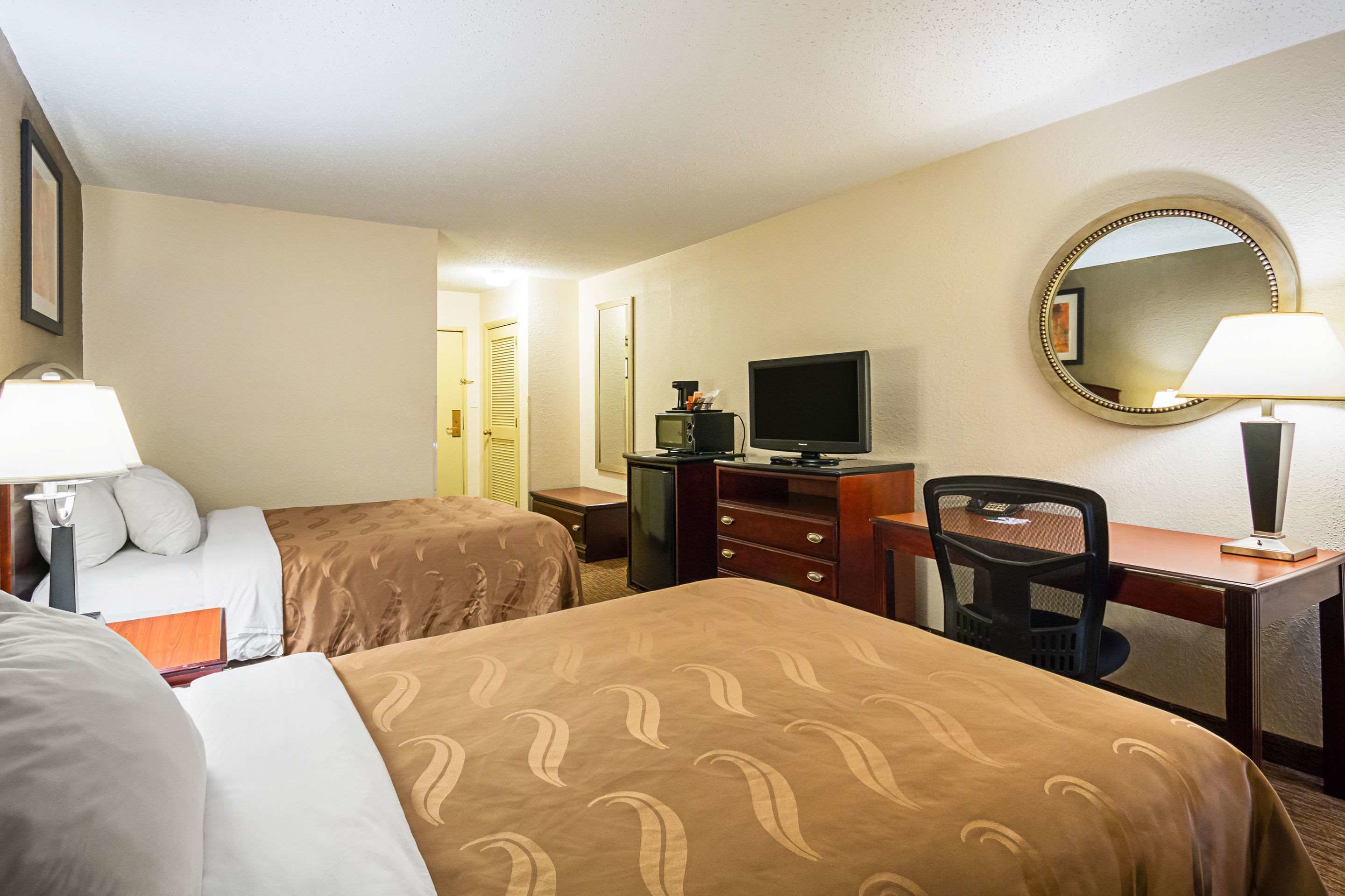 Une chambre d’hôtel avec deux lits, un bureau avec une chaise, une télévision et un miroir.