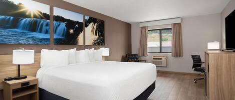 Habitación de hotel con una cama grande, dos mesitas de noche con lámparas, un escritorio con una silla, un ventanal con cortinas y dos cuadros colgados en la pared que representan cascadas.