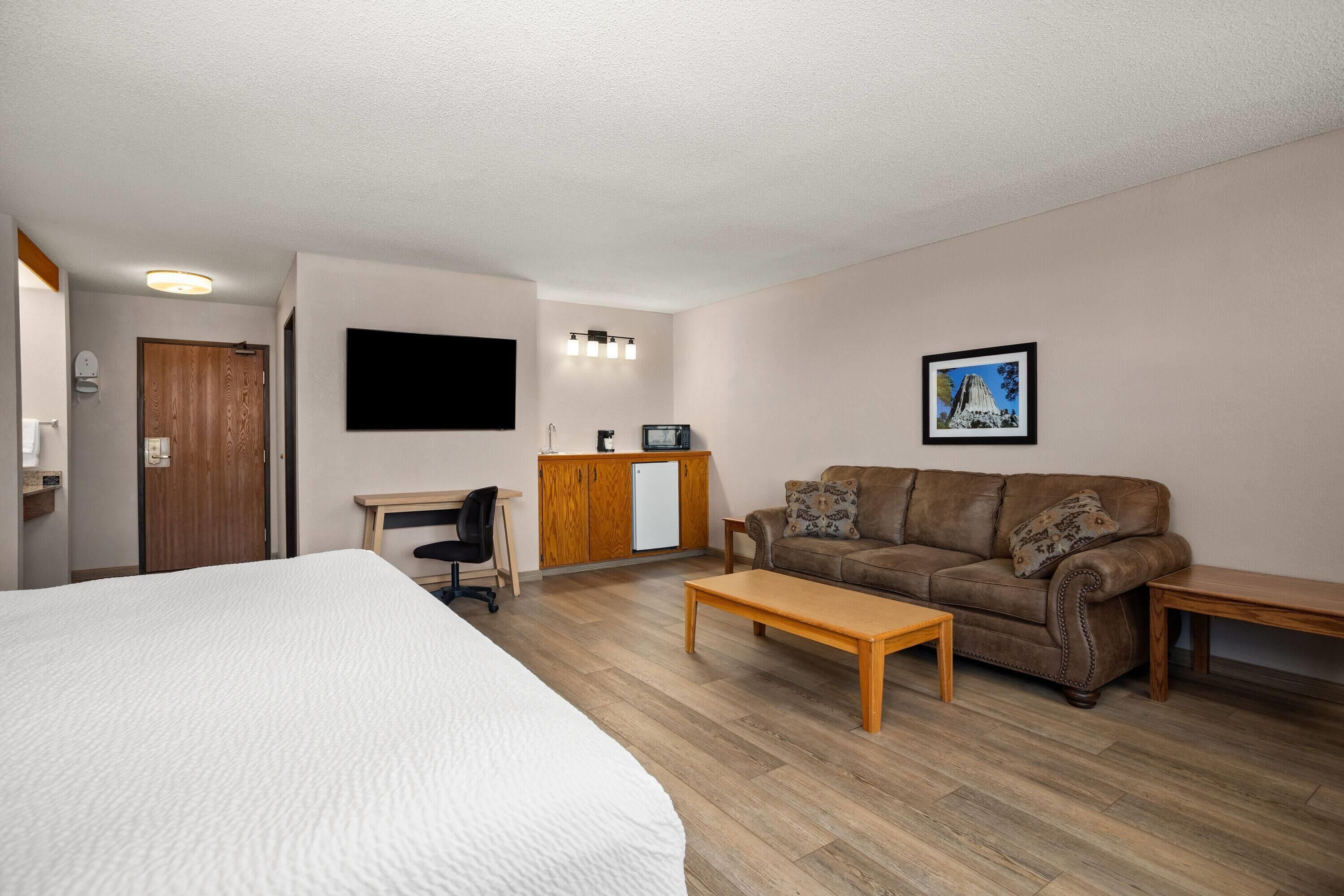 Una habitación de hotel con una cama, un escritorio de madera, un sofá de cuero marrón y una mesa de centro de madera.
